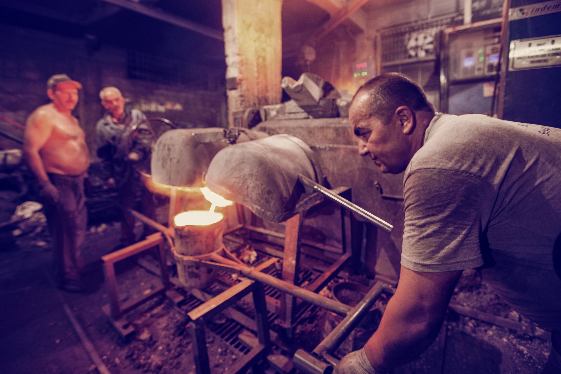 Foundry workers handling a ladle beside molten metal